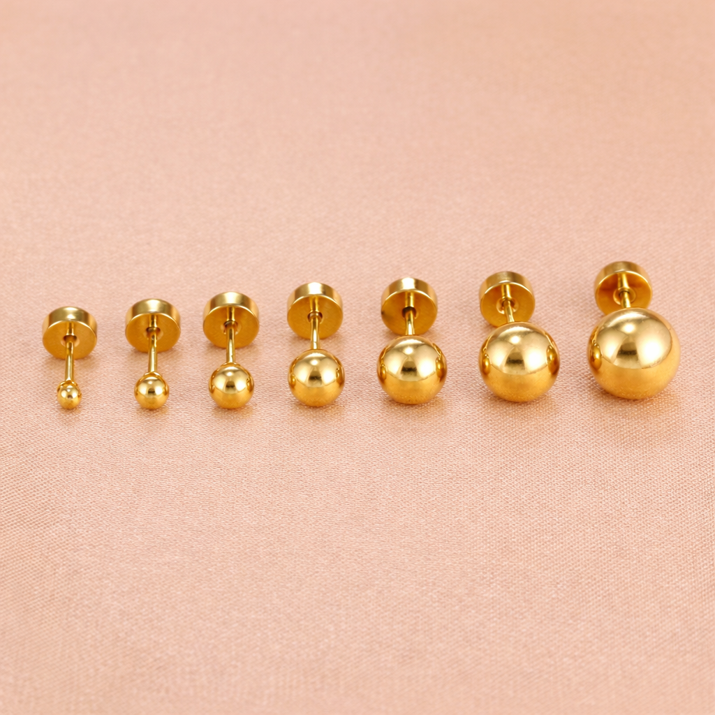 Row of gold ball stud piercings in multiple sizes displayed on a soft fabric background, showing smooth polished finish and flat screw-back closures.