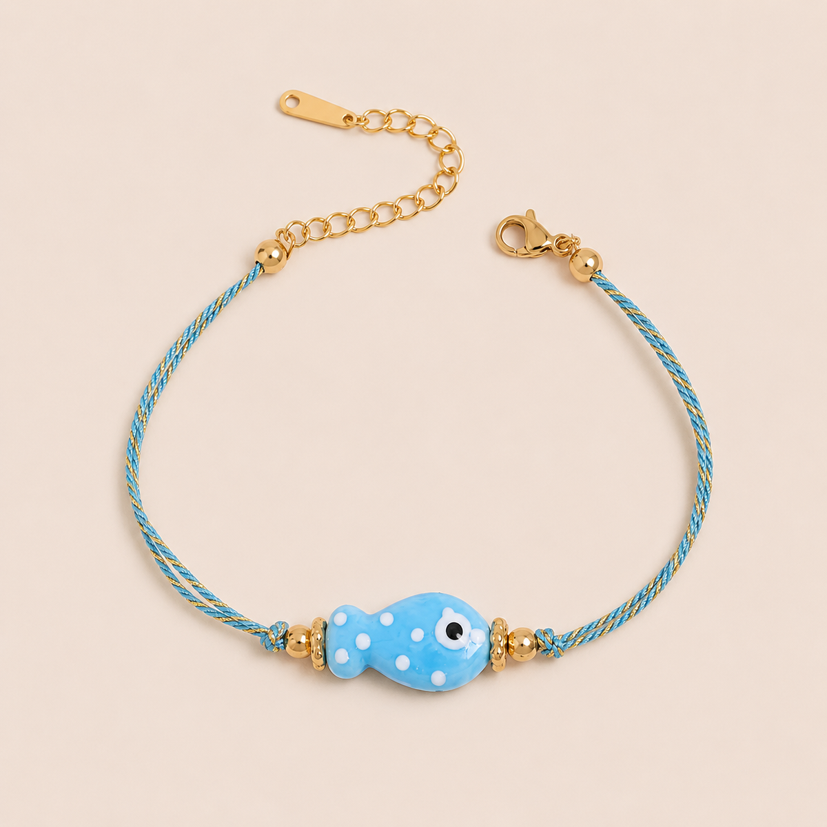 Amalfi BRACELET in blue with a ceramic white polka-dot fish charm on a twisted gold and blue cord, shown flat.