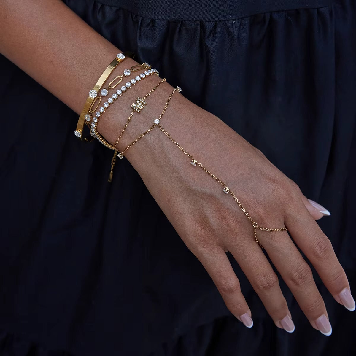 Aura Hand Chain BRACELET worn on the hand layered with several other gold bracelets, model in a black dress.