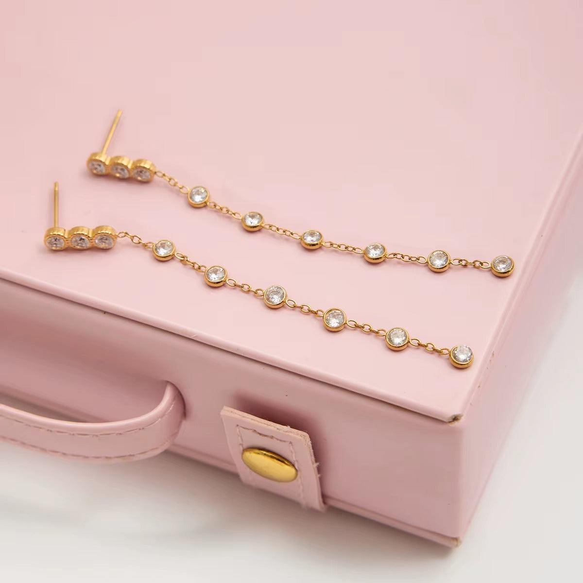 Chamonix Earrings in gold laid on a pink jewelry box, showing the graduated crystal chain drop design.