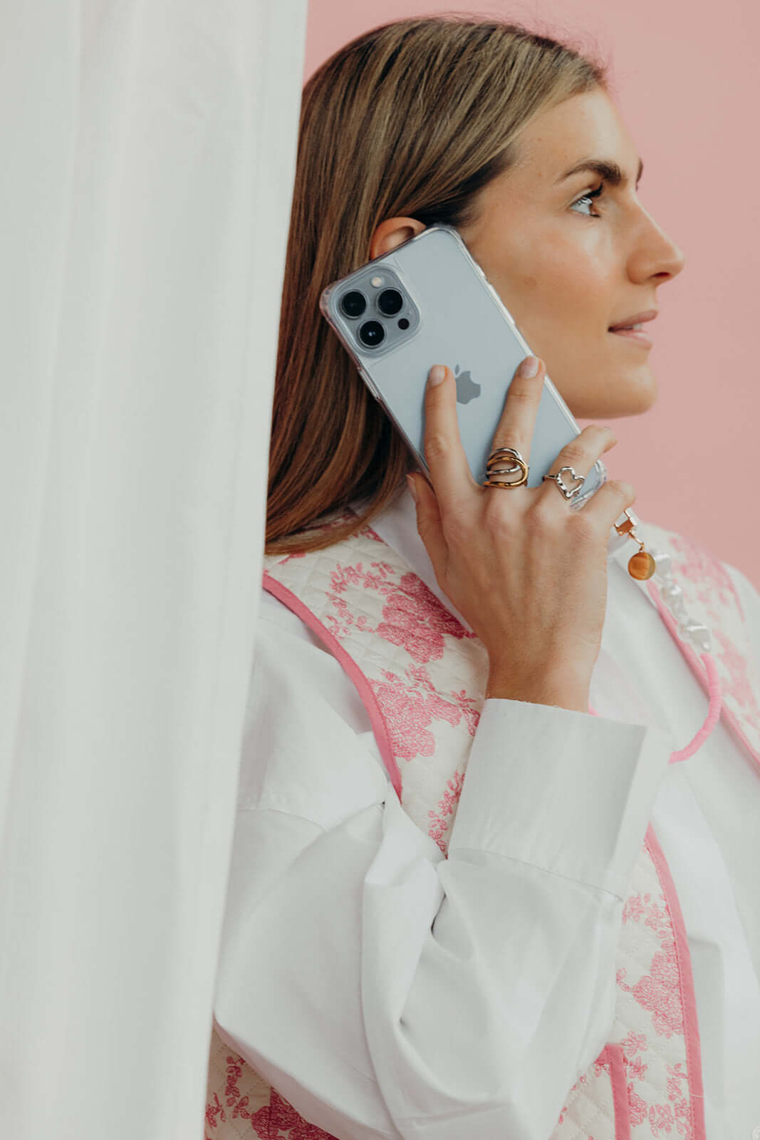 Model in a pink and white floral jacket holds her phone in a clear Classic iPHONE CASE against a pastel pink background.