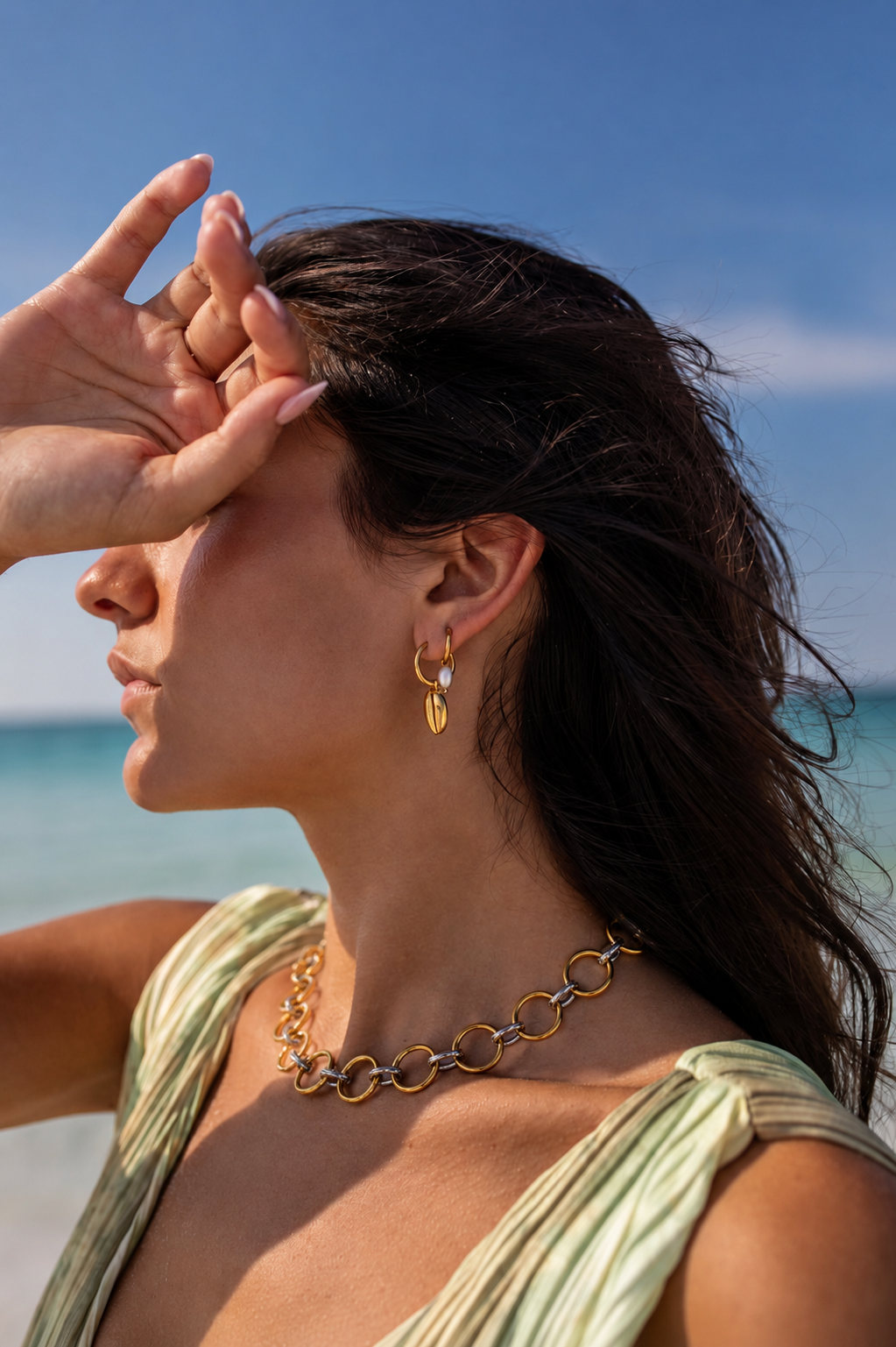 Model wears the two-tone Contradiction NECKLACE with its linked gold and silver circles close to the neckline, by the sea.