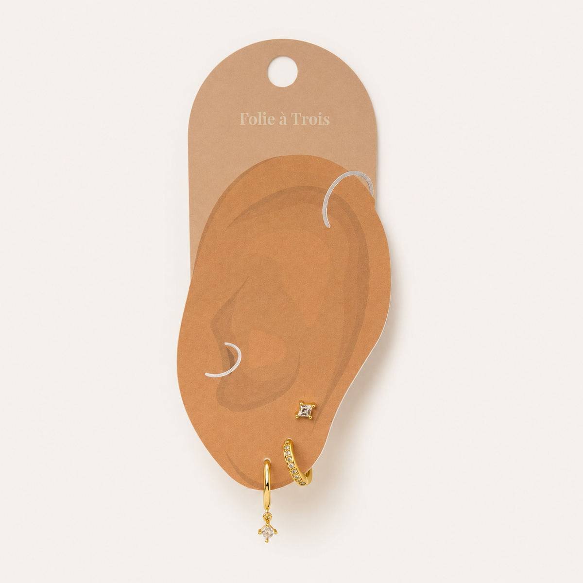 Illustrated Folie a Trois earring card showing the Eira Set pieces arranged on an ear-shaped display, hoop, huggie, and stud.