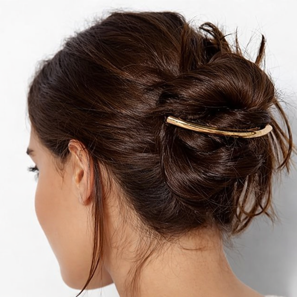 Gia HAIR CLIP in gold-tone metal, worn holding a messy twisted bun on brunette hair, side view.