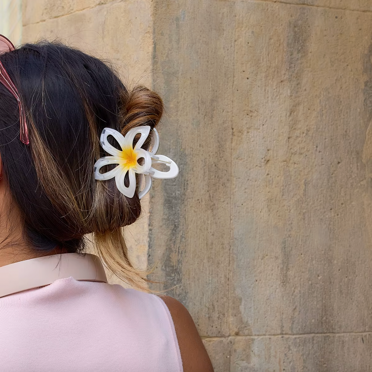 Hawaii HAIR CLIP worn in a low bun on dark hair, white flower clip, model against a stone wall.