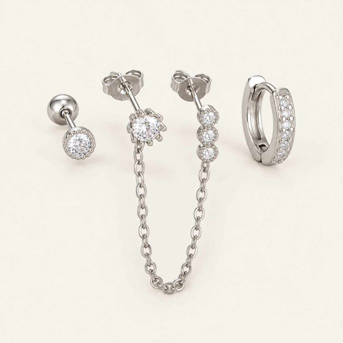 The Folie à Trois Ines SET in silver: a bezel stud, a bezel stud linked by chain to three small drops, and a pavé huggie hoop.