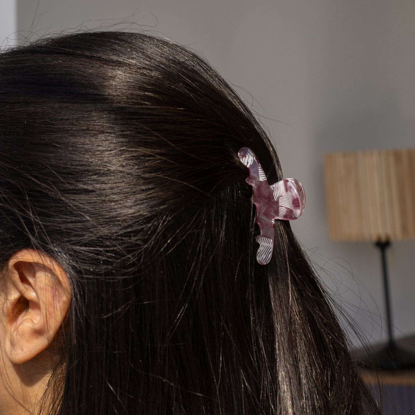 Iris HAIR CLIP in a purple and white striped pattern, worn half-up on dark hair, side view with a lamp in the background.