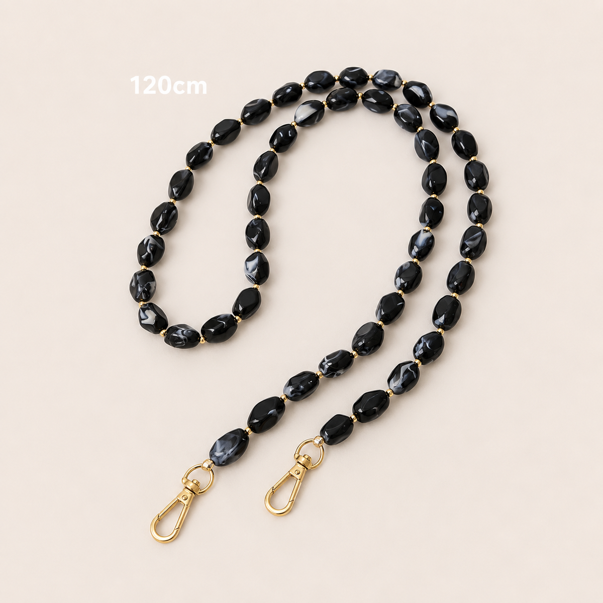Folie à Trois Isolde long wholesale phone chain in black marbled beads with gold accent beads and gold clasps, laid flat on a cream background.