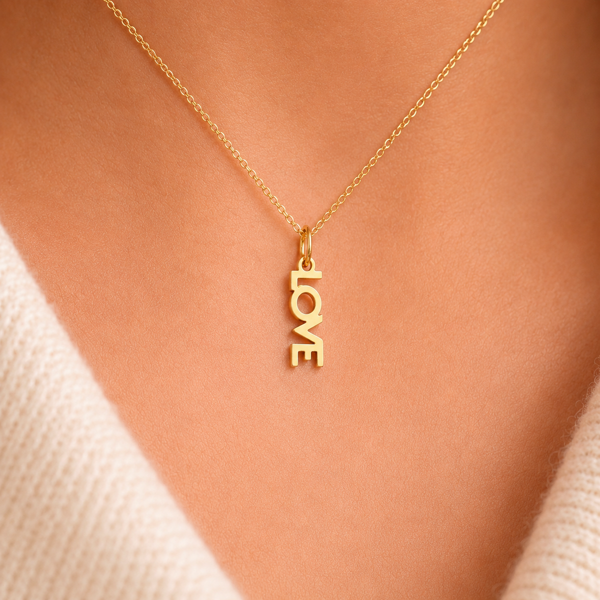 The Love CHARM worn on a fine gold chain at the neckline, styled with a cream sweater in close-up light.