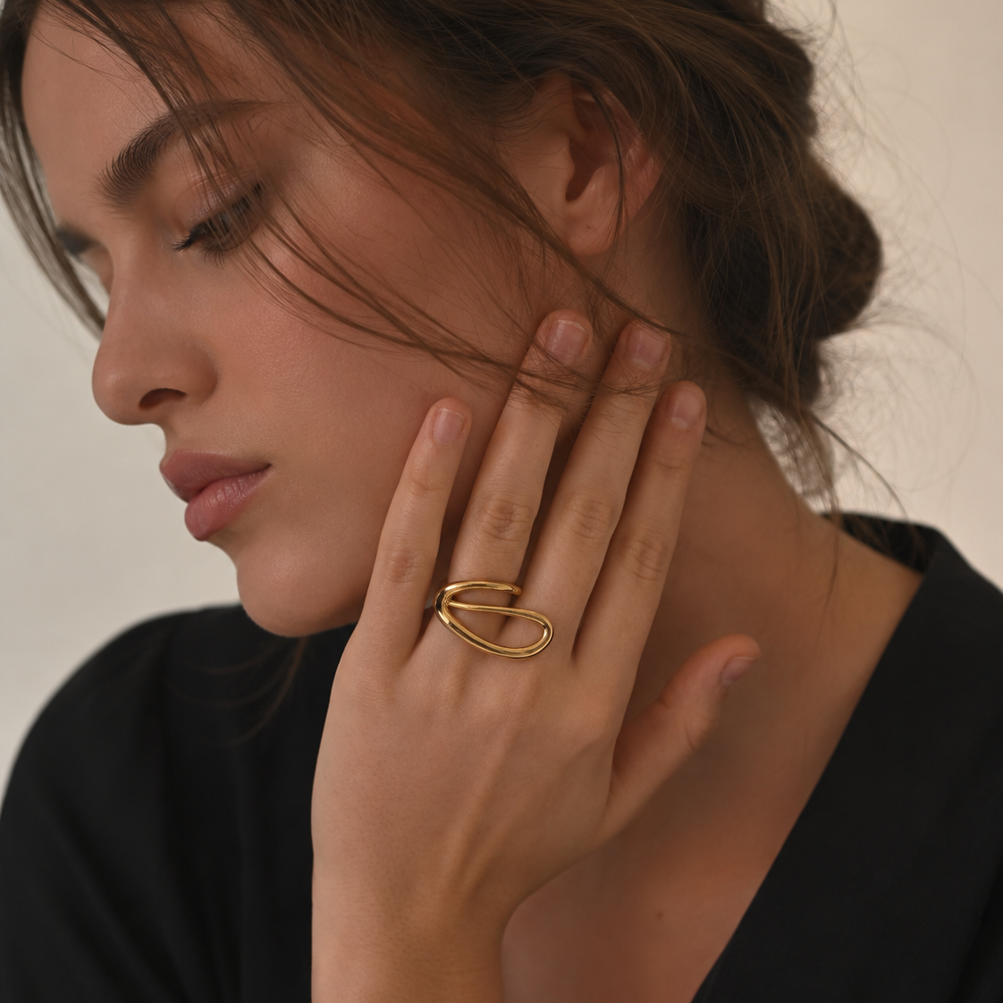 Model wears the gold Solstice RING's looping oval spiral on her finger, hand raised to her cheek.