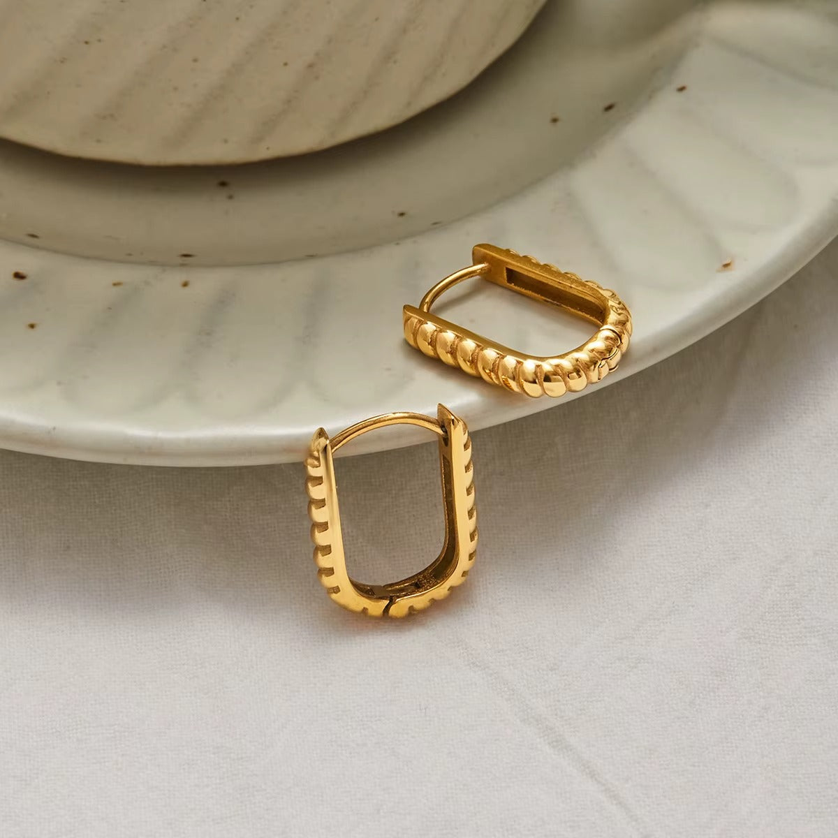 Another angle of the St. Moritz Earrings, highlighting the ribbed texture and oval hoop shape of the gold design on the same plate.