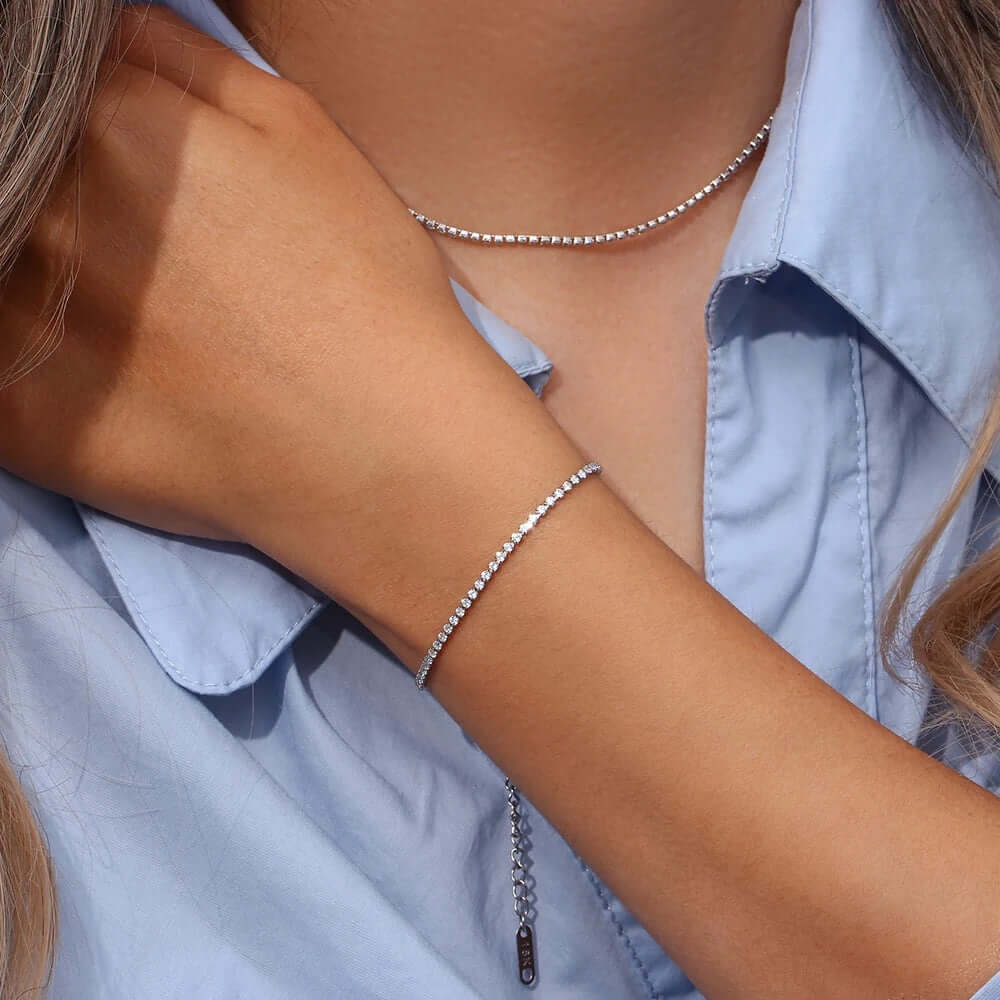 The Tennis NECKLACE in silver worn close at the neckline, paired with a matching tennis bracelet on the raised wrist.