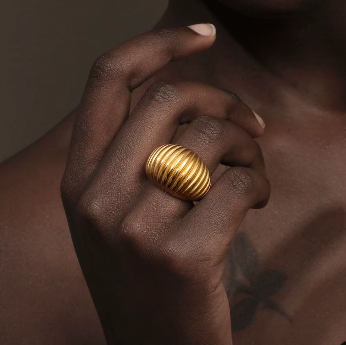 Close-up of a hand near the collarbone wearing the chunky gold ribbed Zelma RING, warm dramatic lighting.