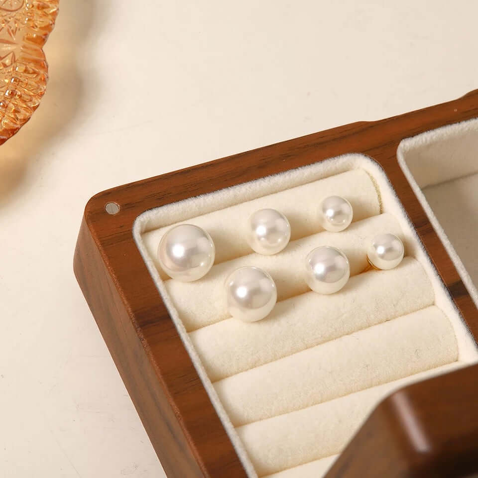 Pearl Me Earrings line up in a wooden ring box, showing five sizes of round pearl studs side by side.