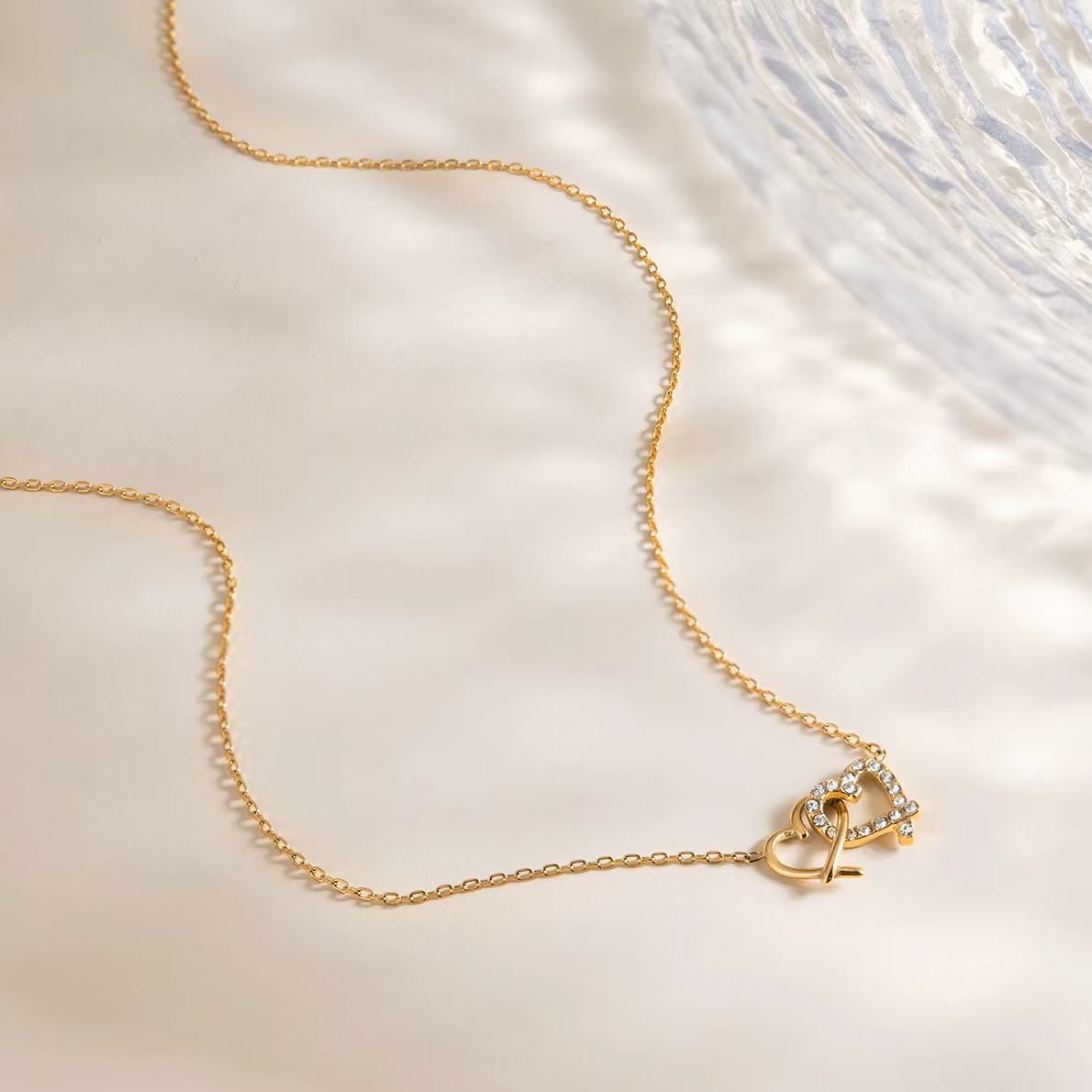 Gold-plated necklace with a delicate chain and interlocking heart-shaped pendant embellished with clear crystals