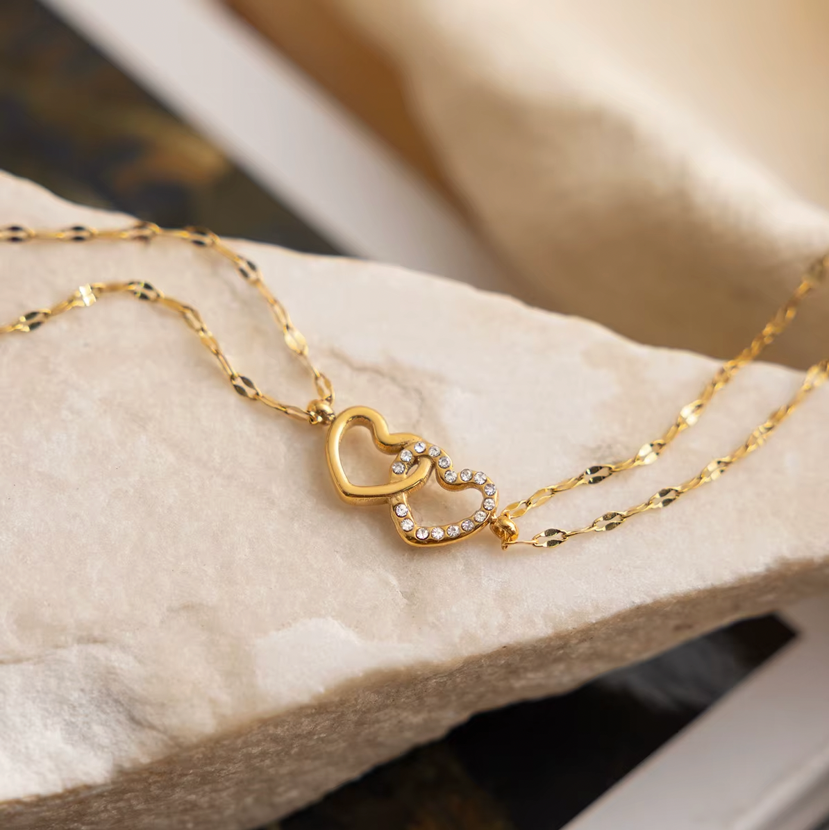 Gold-plated double-chain bracelet with two intertwined heart charms, one polished and one set with clear crystal stones