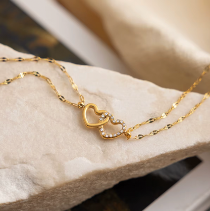 Gold-plated double-chain bracelet with two intertwined heart charms, one polished and one set with clear crystal stones