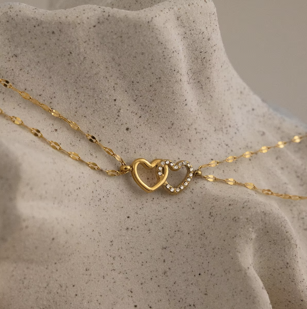 Gold-plated double-chain bracelet with two intertwined heart charms, one polished and one set with clear crystal stones