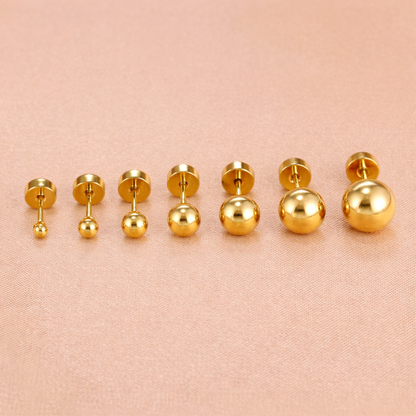 Row of gold ball stud piercings in multiple sizes displayed on a soft fabric background, showing smooth polished finish and flat screw-back closures.