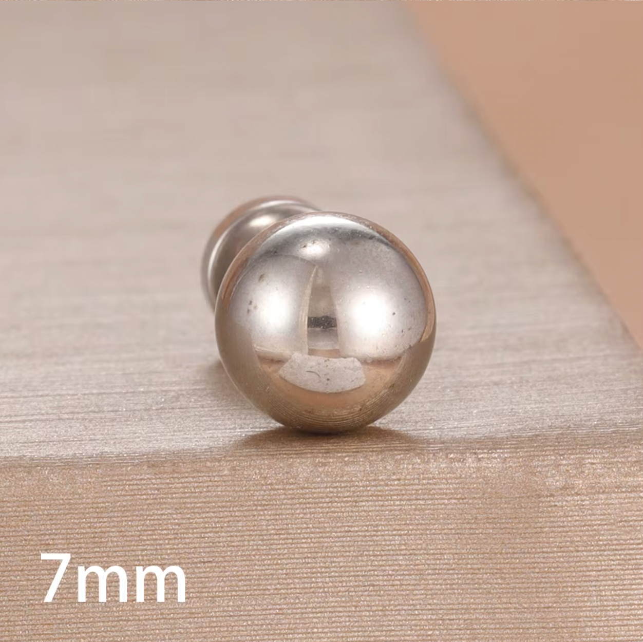 Row of gold ball stud piercings in multiple sizes displayed on a soft fabric background, showing smooth polished finish and flat screw-back closures.