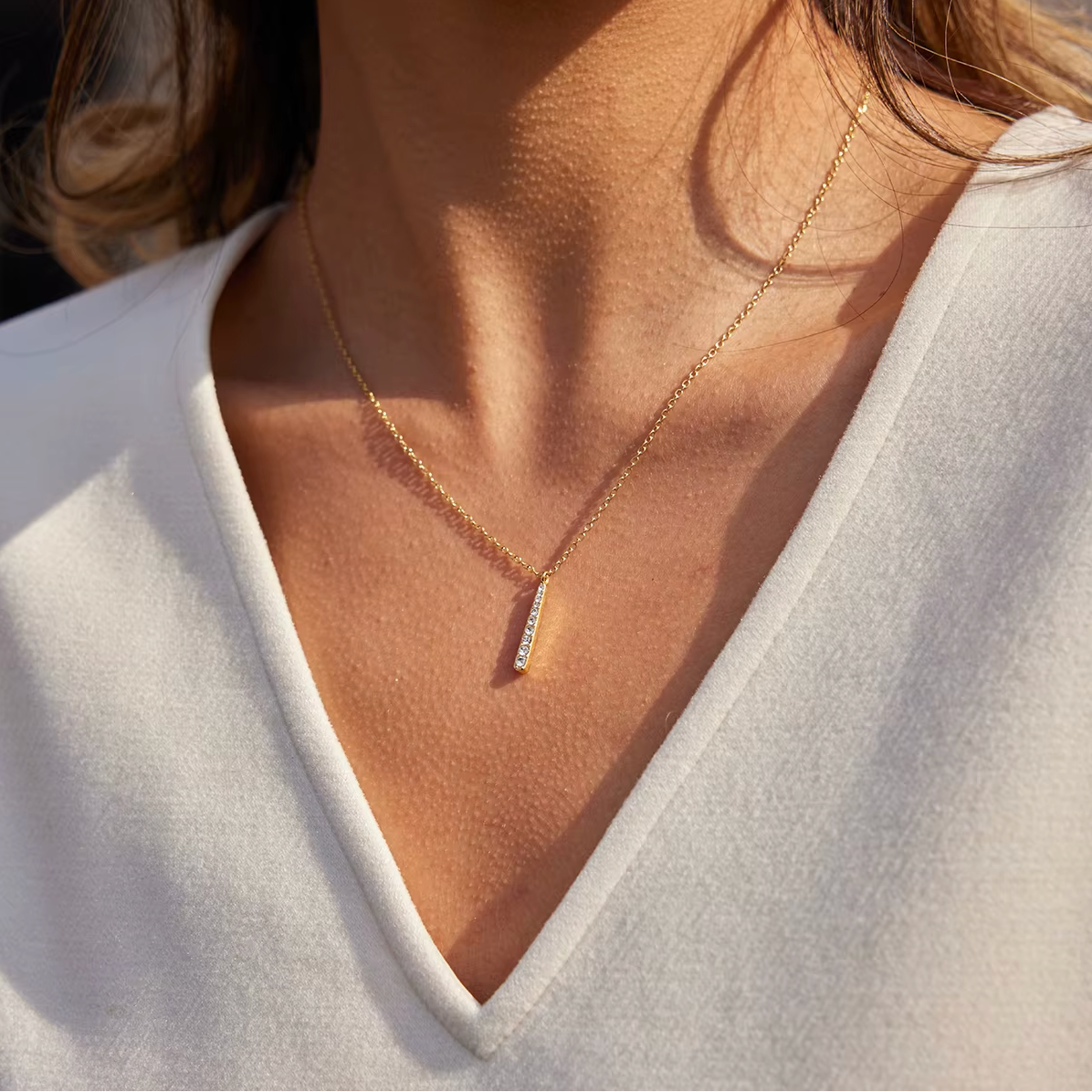 Gold-plated necklace with a fine chain and a slim vertical bar pendant set with clear crystal stones