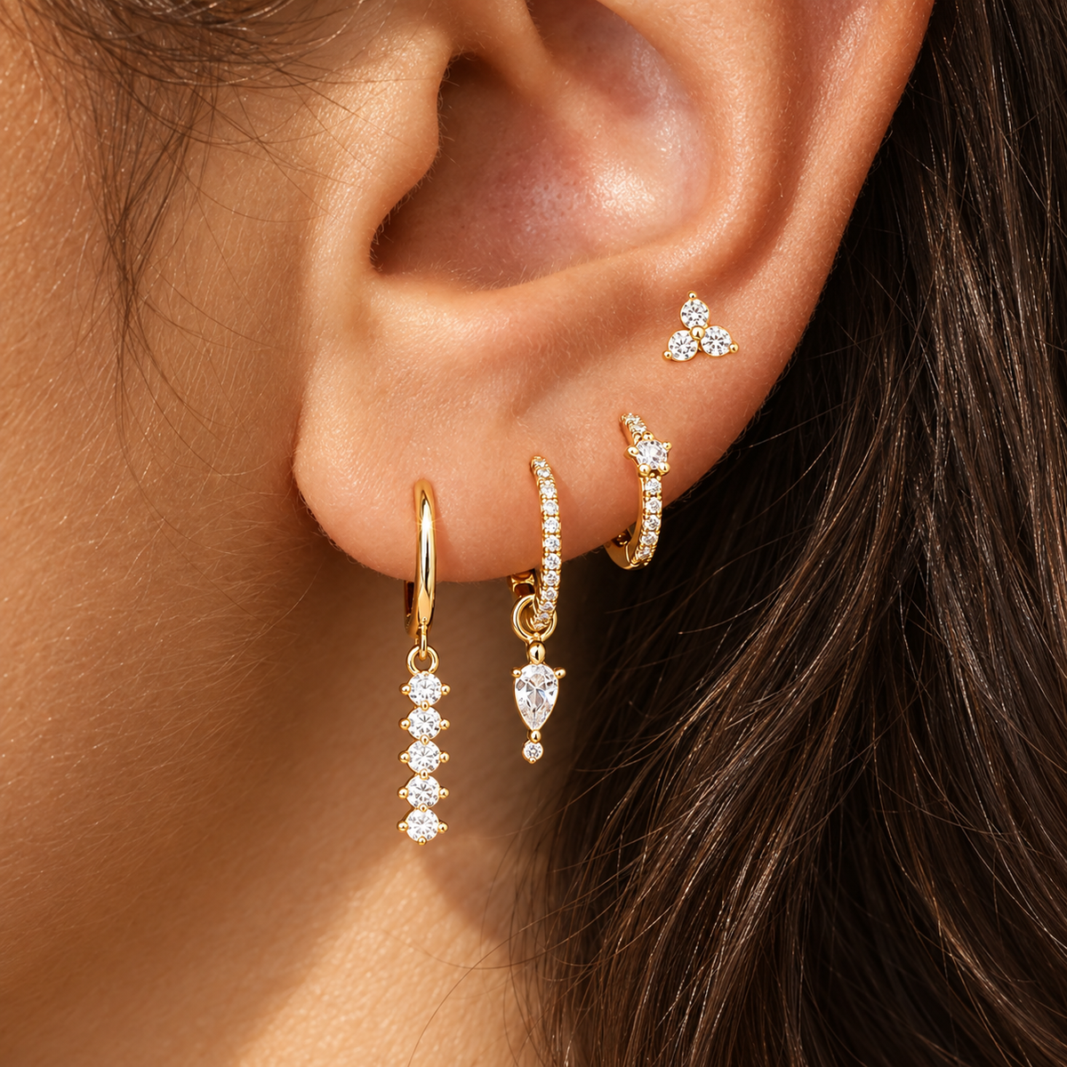 Close-up of an ear stacked with the gold Adele SET: a trio stud, a pavé huggie with pear drop, a crystal hoop and a beaded dangle hoop.