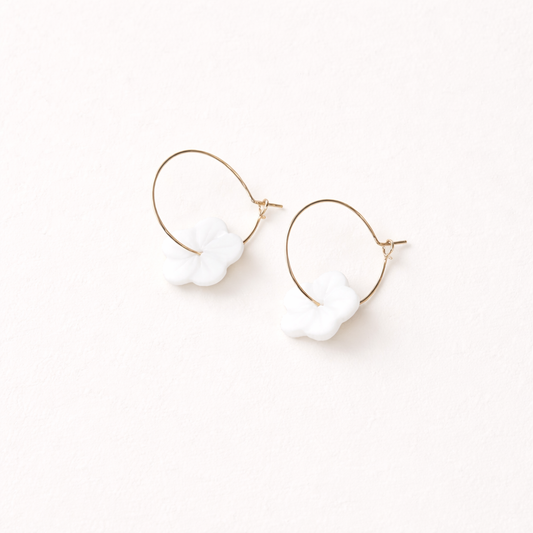 After Glow Earrings string a white flower-shaped bead onto a thin gold wire hoop for a light, airy look.