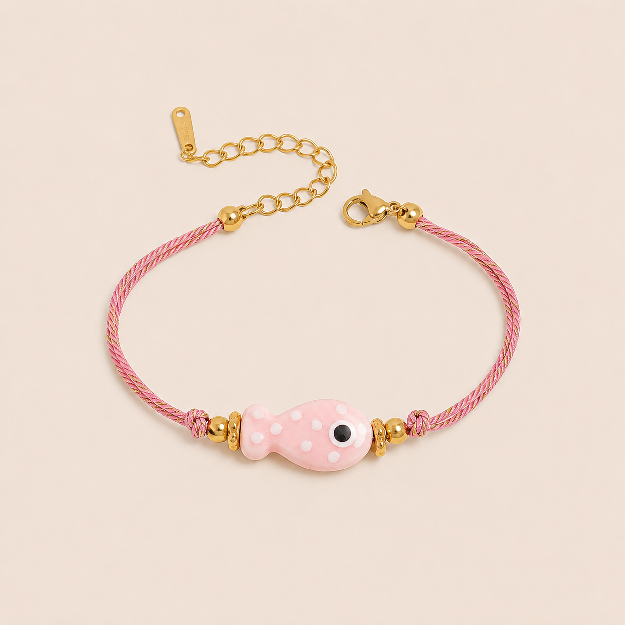 Amalfi BRACELET in pink with a ceramic white polka-dot fish charm on a twisted gold and pink cord, shown flat.