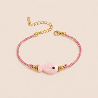Amalfi BRACELET in pink with a ceramic white polka-dot fish charm on a twisted gold and pink cord, shown flat.