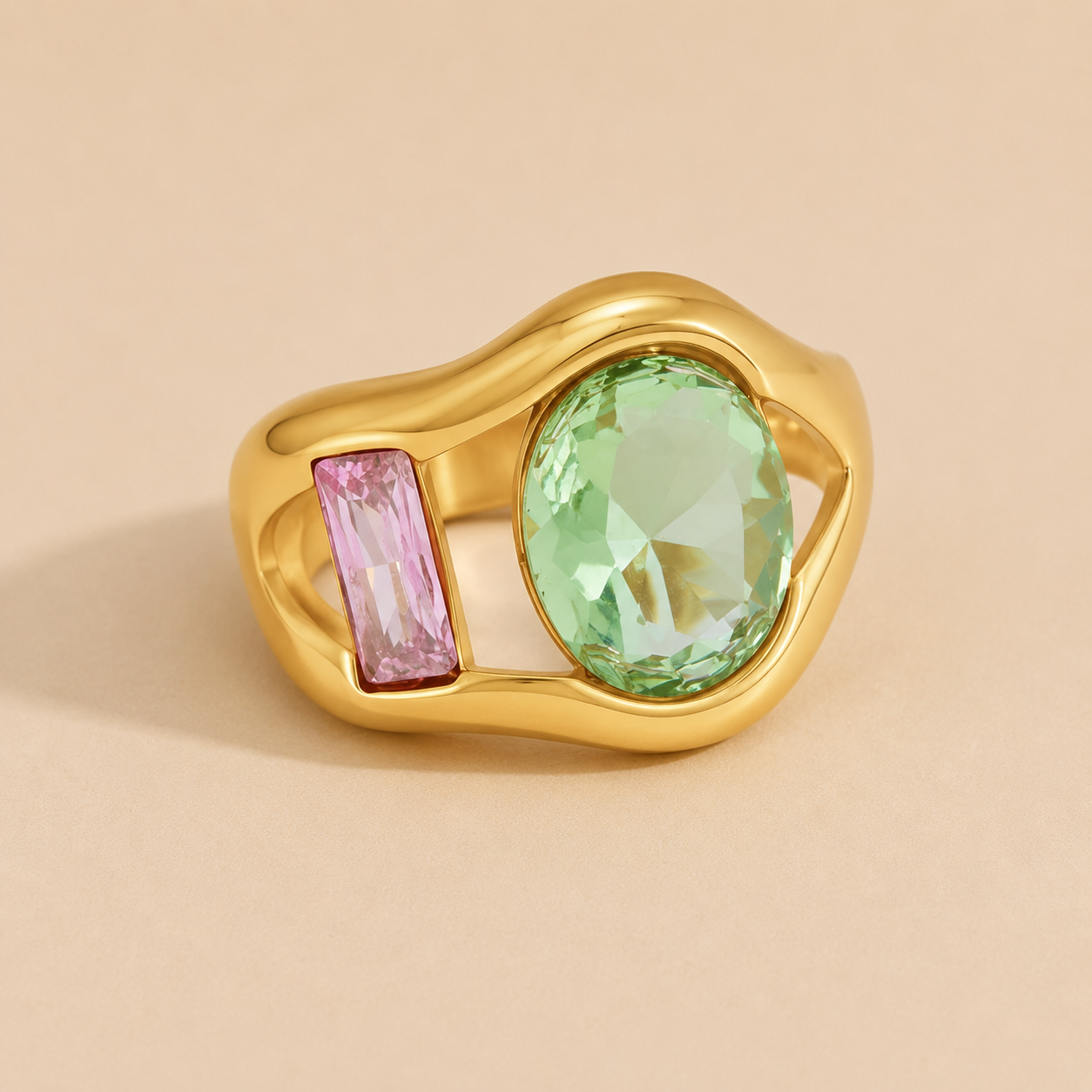 Gold ring set with a green oval stone and a pink baguette-cut stone side by side, on a beige backdrop — Folie à Trois Amara RING.