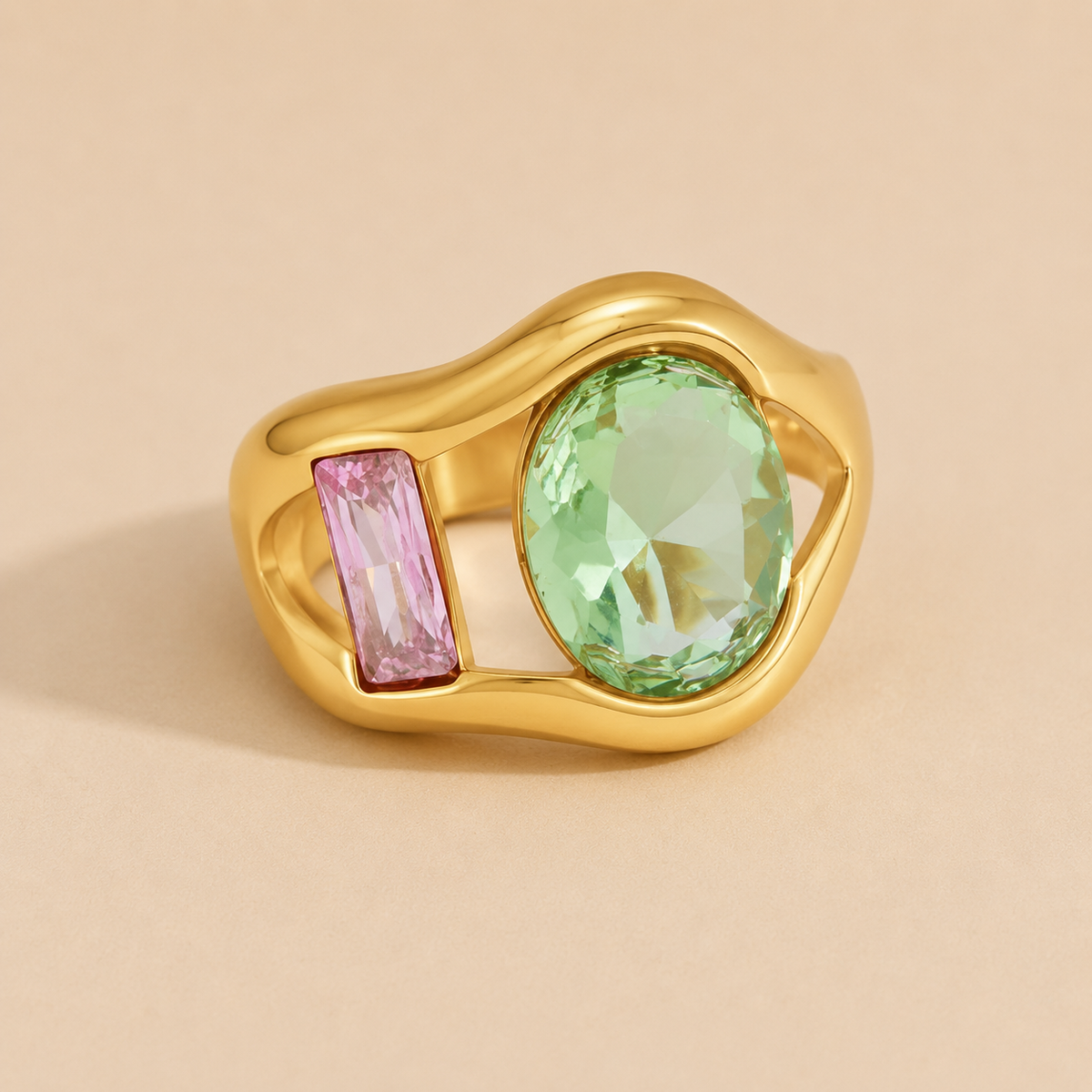 Gold ring set with a green oval stone and a pink baguette-cut stone side by side, on a beige backdrop — Folie à Trois Amara RING.