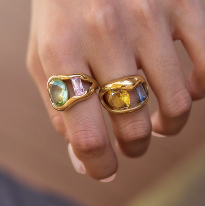 Close-up of two Amara RING colorways stacked on a model's finger, one set with green and pink stones, the other with yellow and blue stones.