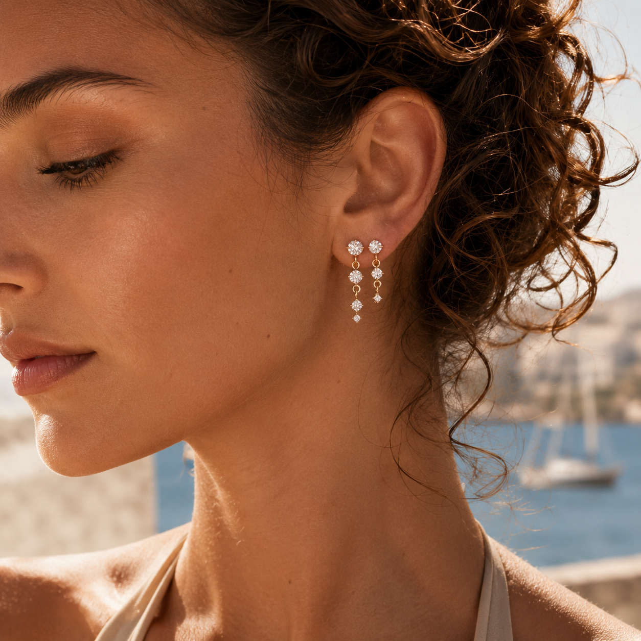 Close-up of a model wearing the gold Andromeda EARRINGS, a graduated line of three round cubic zirconia stones.