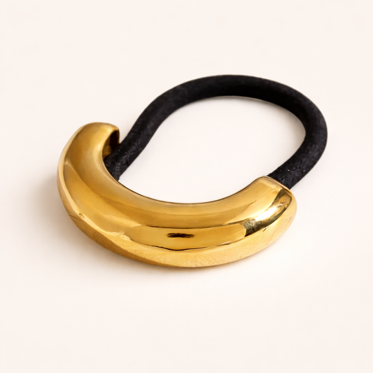 Anita Hair Tie chunky gold sculptural bead on a black elastic band, studio flat-lay on cream.