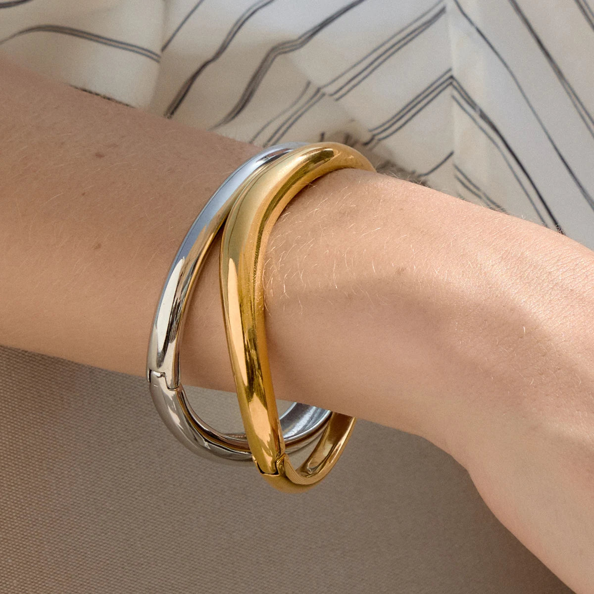 Wrist stacked with gold and silver-tone Arco BRACELETS, sleek polished bangles with a striped shirt — Folie à Trois