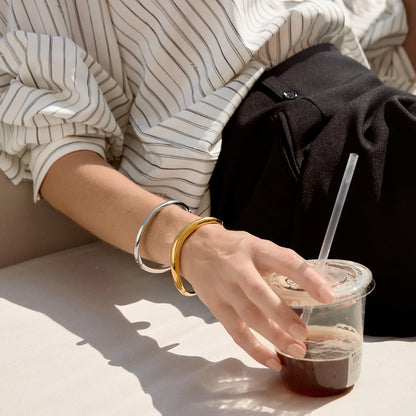 Woman in a striped shirt holding an iced coffee, wearing silver-tone and gold Arco BRACELETS — Folie à Trois