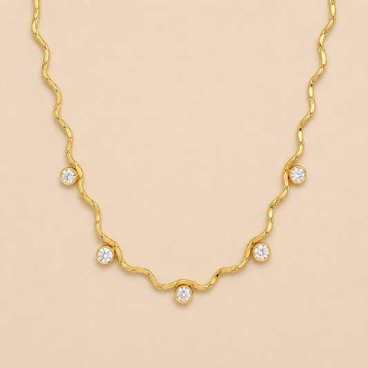 Gold wavy chain necklace with bezel-set crystal stations from the Aria NECKLACE design, laid flat on a beige background.