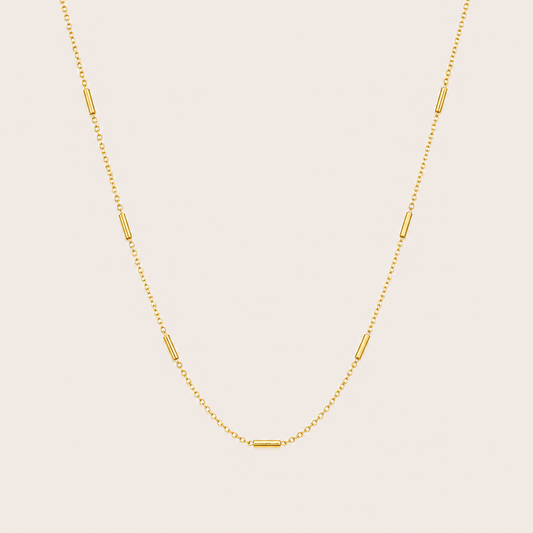 Gold chain necklace with small tube station beads spaced along the length, the Asta NECKLACE, shown in a close-up studio shot.