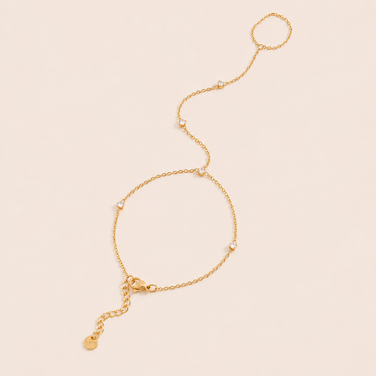 Aura Hand Chain BRACELET in gold with small bezel-set crystal stations linking the wrist chain to a ring, shown flat.