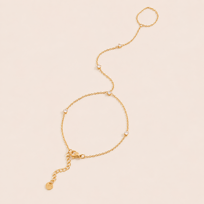 Aura Hand Chain BRACELET in gold with small bezel-set crystal stations linking the wrist chain to a ring, shown flat.