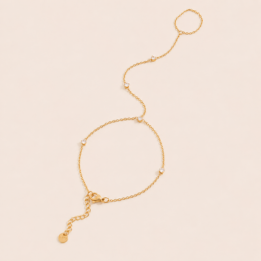 Aura Hand Chain BRACELET in gold with small bezel-set crystal stations linking the wrist chain to a ring, shown flat.