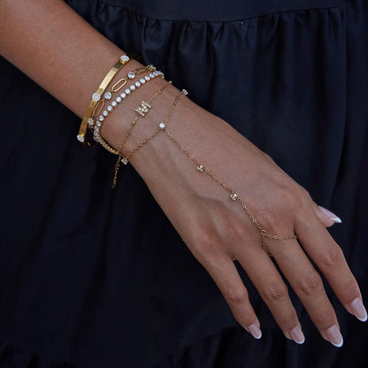 Aura Hand Chain BRACELET worn on the hand layered with several other gold bracelets, model in a black dress.