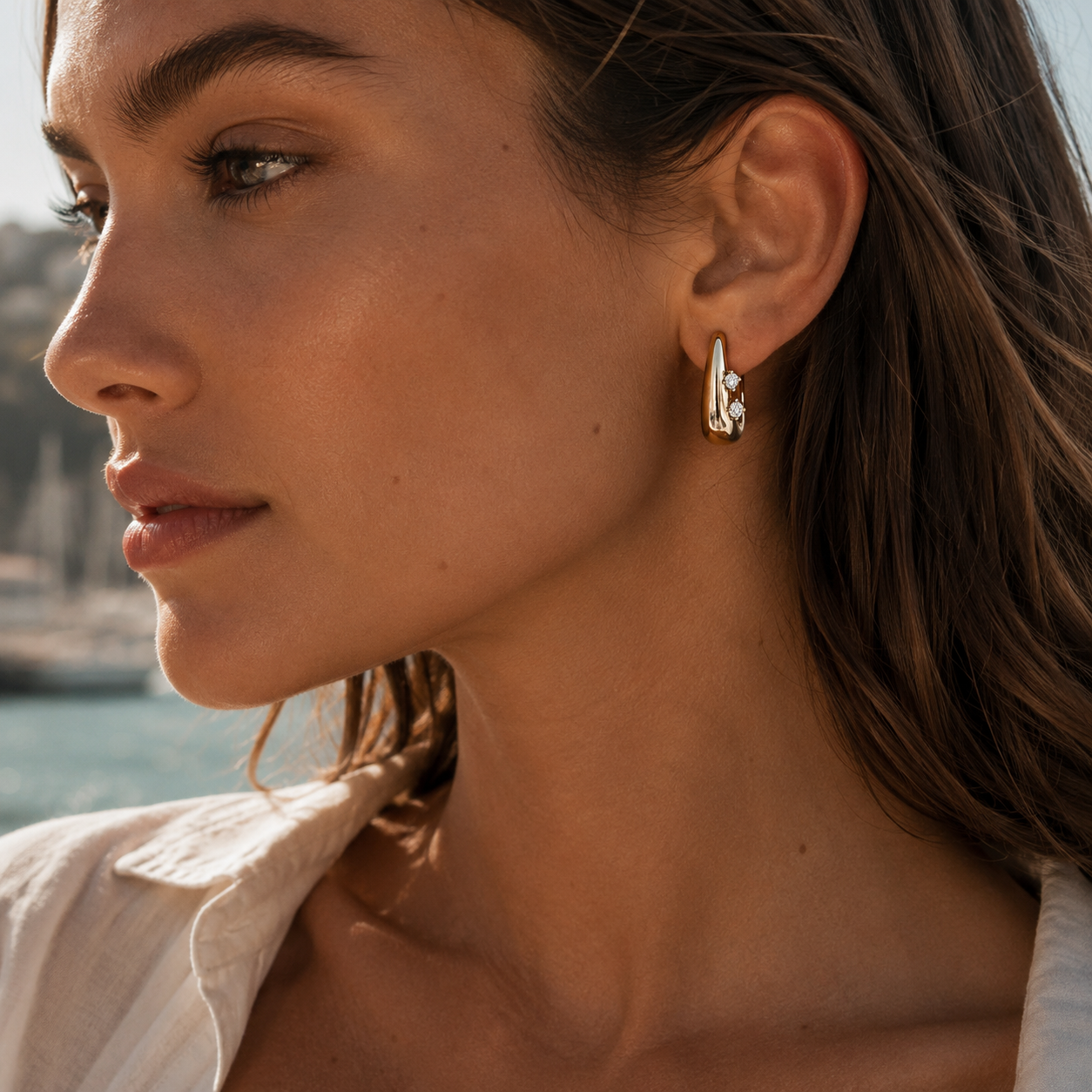 A model wears a gold Avaline EARRINGS teardrop hoop with two round cubic zirconia stones on her ear.