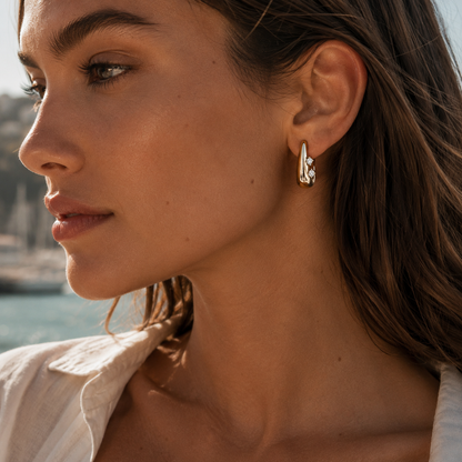 A model wears a gold Avaline EARRINGS teardrop hoop with two round cubic zirconia stones on her ear.