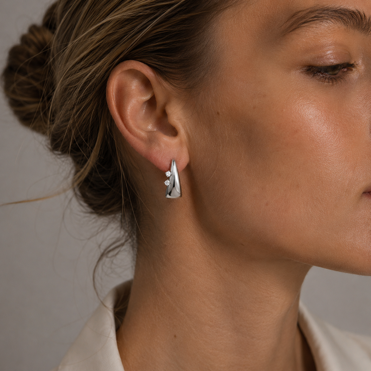 A model wears a silver Avaline EARRINGS teardrop hoop with two round cubic zirconia stones on her ear.