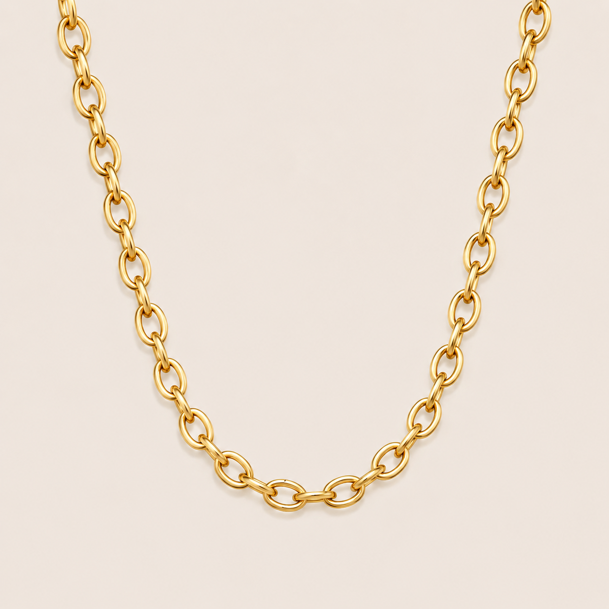 Gold chunky oval-link chain necklace, the Aveline NECKLACE, shown in a close-up studio shot on a soft beige background.