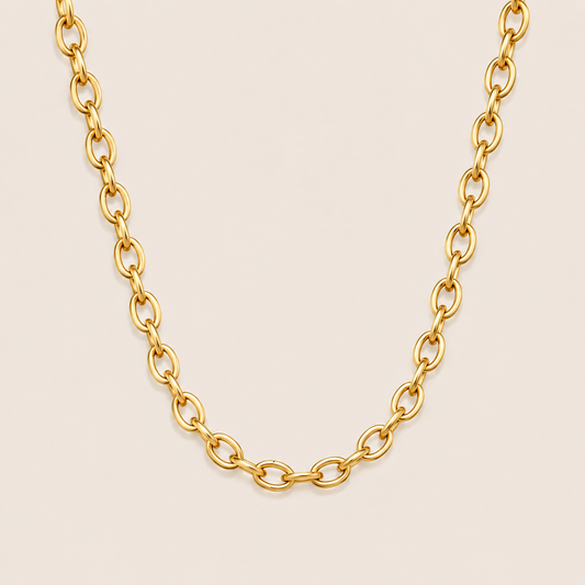 Gold chunky oval-link chain necklace, the Aveline NECKLACE, shown in a close-up studio shot on a soft beige background.