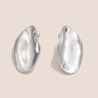 Silver sculptural asymmetric dome stud earrings with a hammered, wavy organic shape on a cream backdrop — Folie à Trois Axis EARRINGS