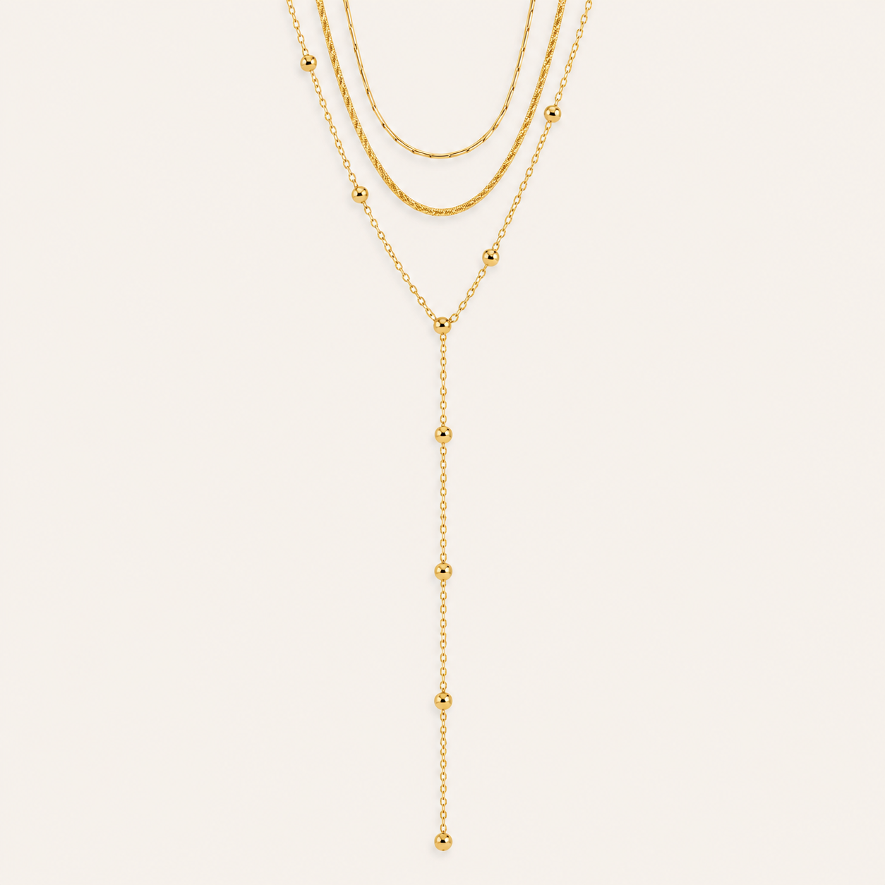 Layered gold Azure Y NECKLACE with a snake chain, a beaded chain and a long ball-bead lariat drop, laid flat on beige.
