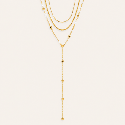 Layered gold Azure Y NECKLACE with a snake chain, a beaded chain and a long ball-bead lariat drop, laid flat on beige.